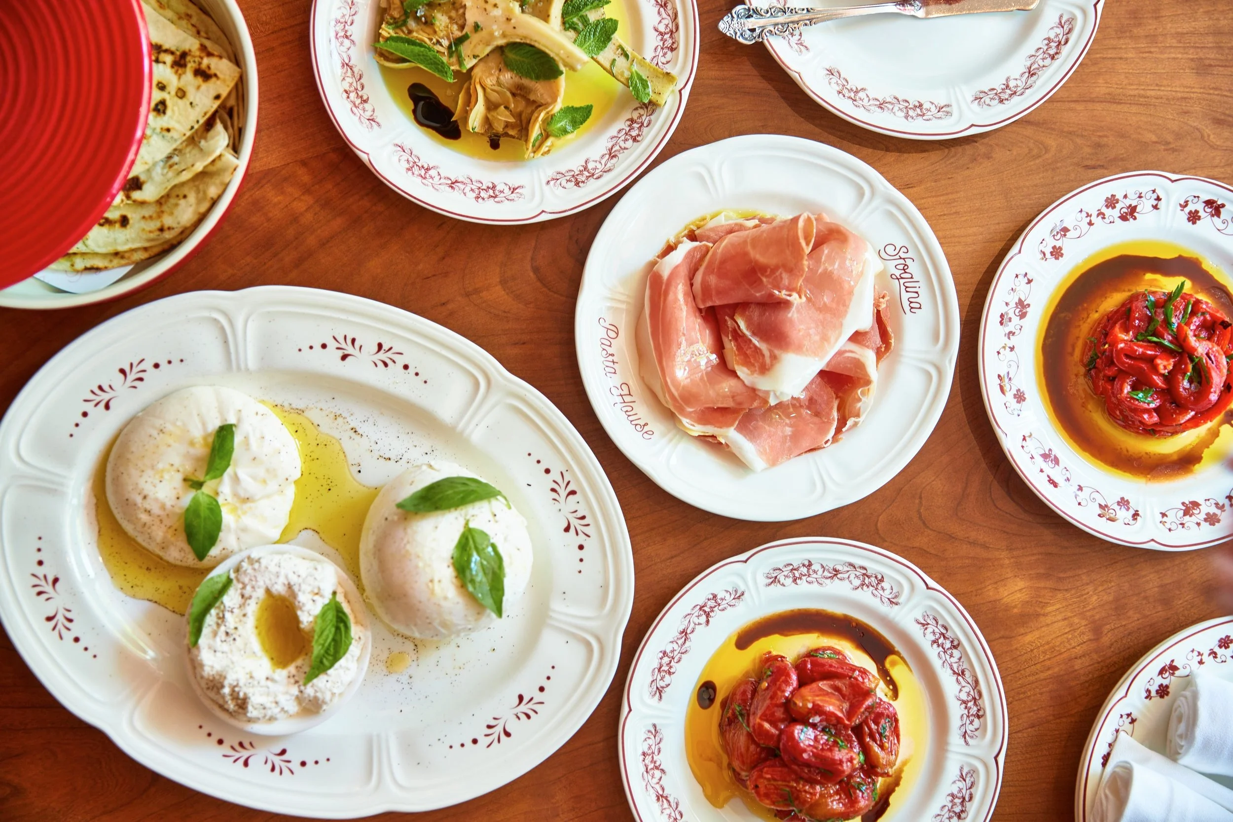 A dinner table filled with Italian dishes, including burrata in olive oil, prosciutto, and sun-dried tomatoes with balsamic glaze.