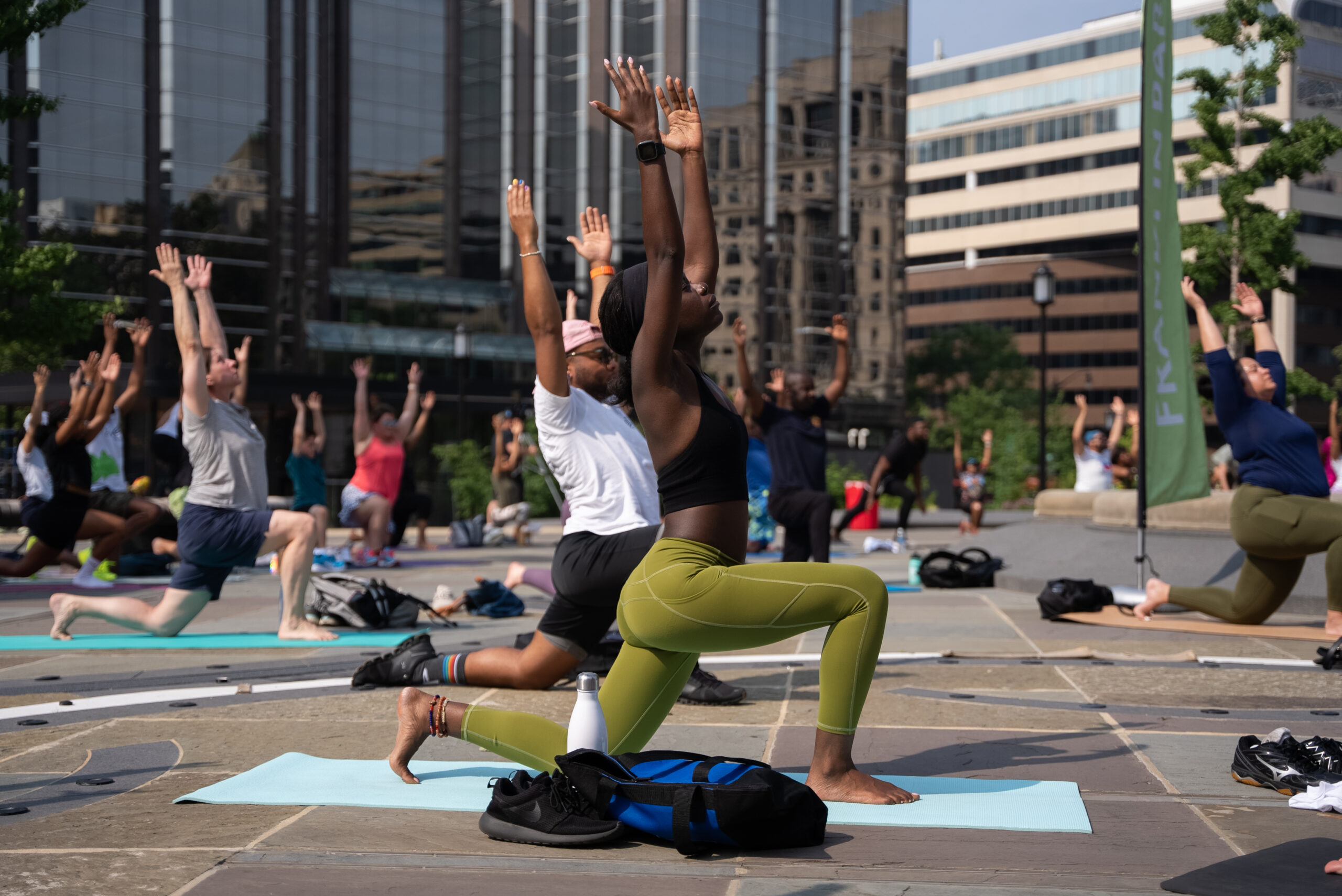 People practicing yoga in a park with hands raised and eyes closed during an outdoor group session.