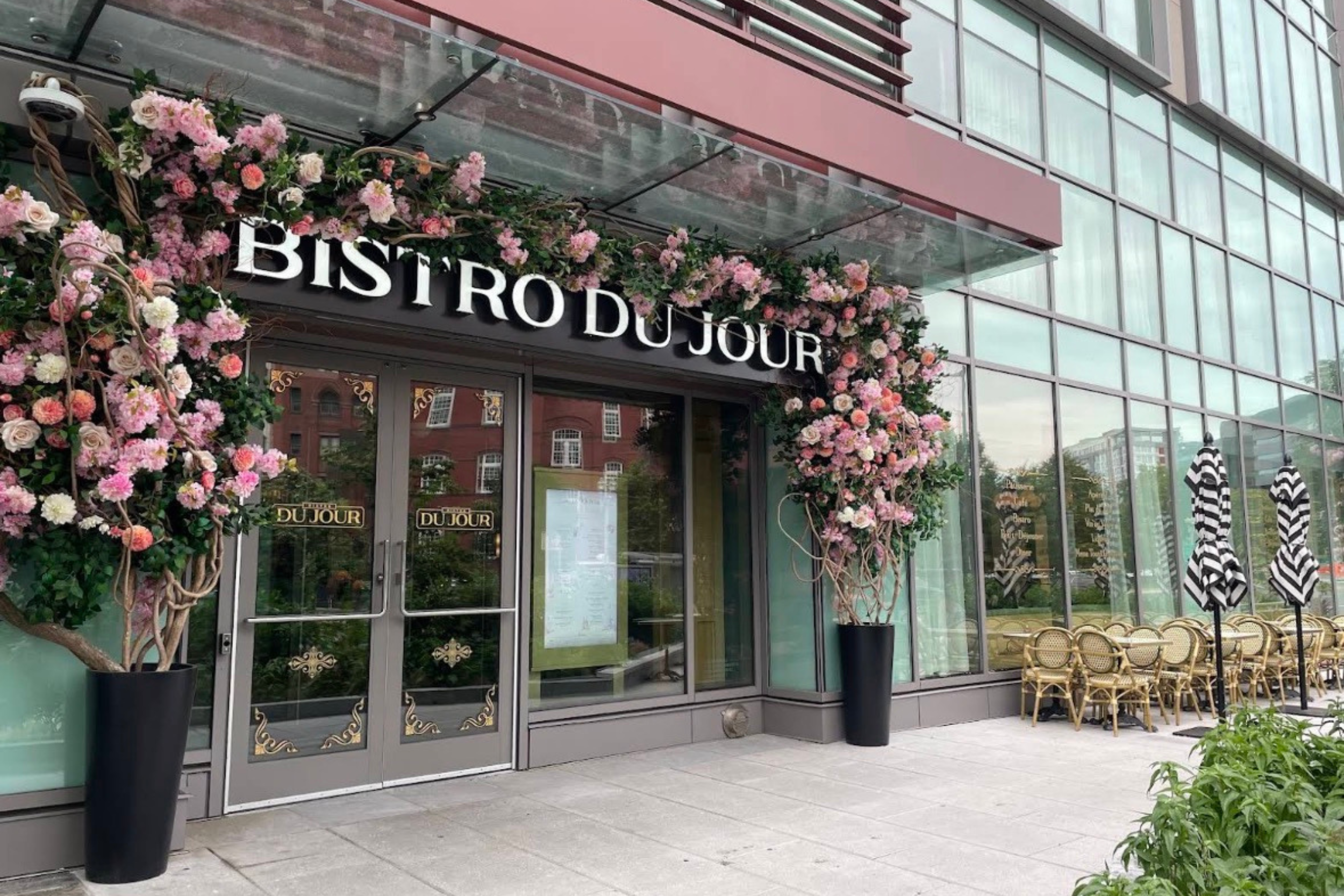 The entrance of BISTRO DU JOUR decorated with pink floral arrangements wrapped around the doorway and restaurant sign.