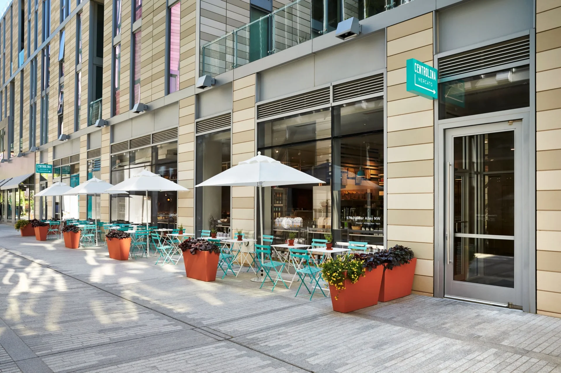 A sunny alleyway with outdoor dining tables, green chairs, and large patio umbrellas in Downtown DC.